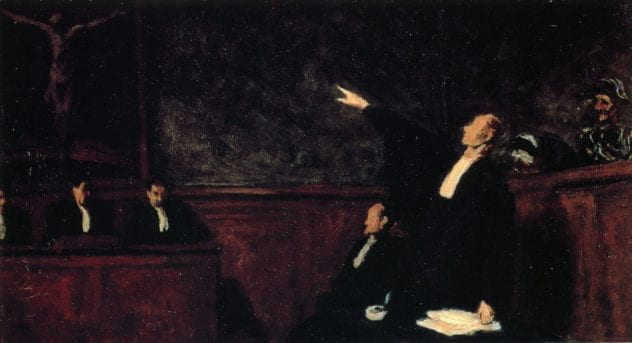 Lawyer standing in court speaking to the court while pointing to the gallery